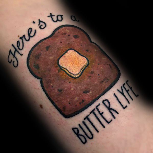 Playful toast tattoo with a melting butter pat and the phrase "Here's to a Butter Lyfe," combining humor with a bold, cartoon-style design.