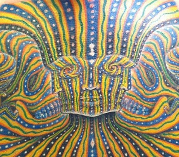 Psychedelic Tool-inspired tattoo with a symmetrical face made of vibrant yellow, green, and blue lines and dotted patterns across the back.