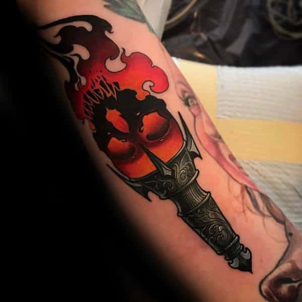 Dark torch tattoo with red and black flames forming a sinister face, paired with a decorative, armor-like handle design.
