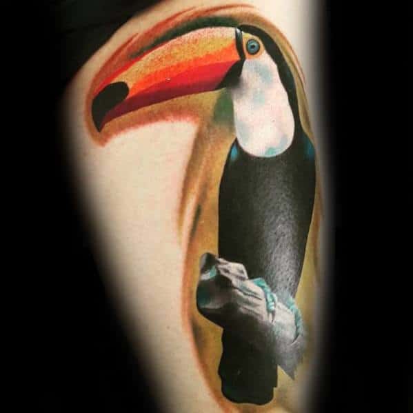 Realistic toucan tattoo with a vivid orange-to-red beak, perched on a branch with soft shading and warm tones on the upper arm.