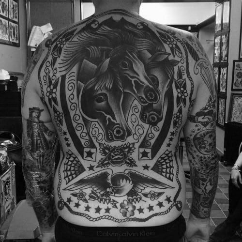 Full back tattoo in traditional style featuring three horse heads inside a large horseshoe, surrounded by stars, flowers, and bold motifs.