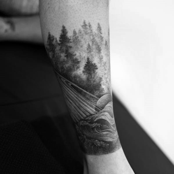 Black ink nature tattoo on the leg, featuring a misty forest, a flowing river, and a setting sun, creating a serene and detailed landscape design.