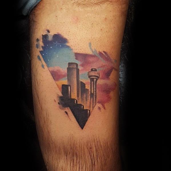 Vibrant Dallas skyline tattoo with a triangular frame, set against a colorful sunset sky in pink, blue, and purple watercolor tones.