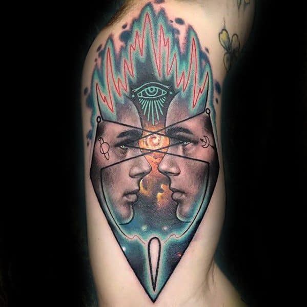 Surreal upper arm tattoo of two mirrored female faces within a triangular frame, featuring a cosmic background and an all-seeing eye above.