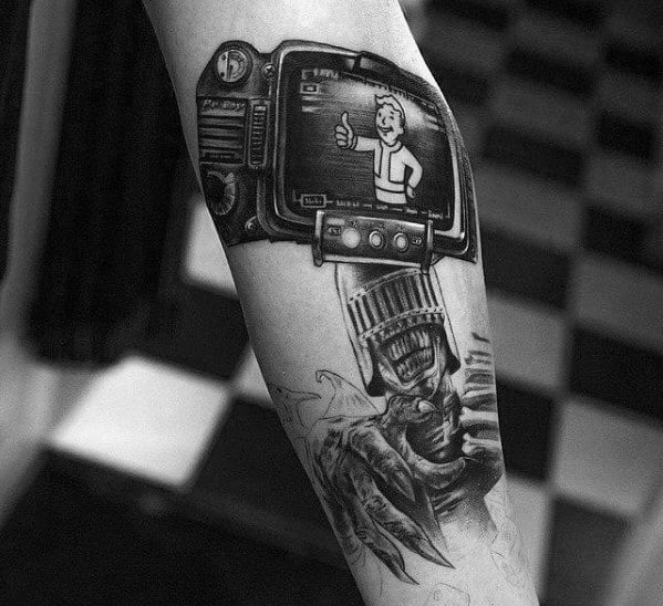 Realistic black and grey tattoo of a Pip-Boy screen showing Vault Boy with a thumbs-up, paired with detailed mechanical and claw imagery.