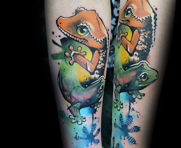 Colorful gecko tattoo on forearm with bold outlines, watercolor splashes in orange, green, and blue, and playful cartoon-like eyes.