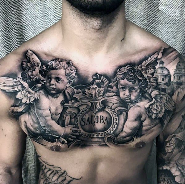 Black and grey chest tattoo featuring two detailed cherubs holding an ornate plaque with the name "Saliba," surrounded by baroque-style architecture.