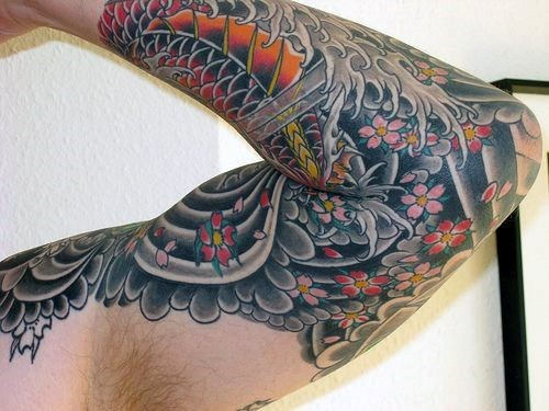 Japanese-style sleeve tattoo featuring intricate cherry blossoms, a vibrant koi fish, swirling waves, and detailed black and grey shading
