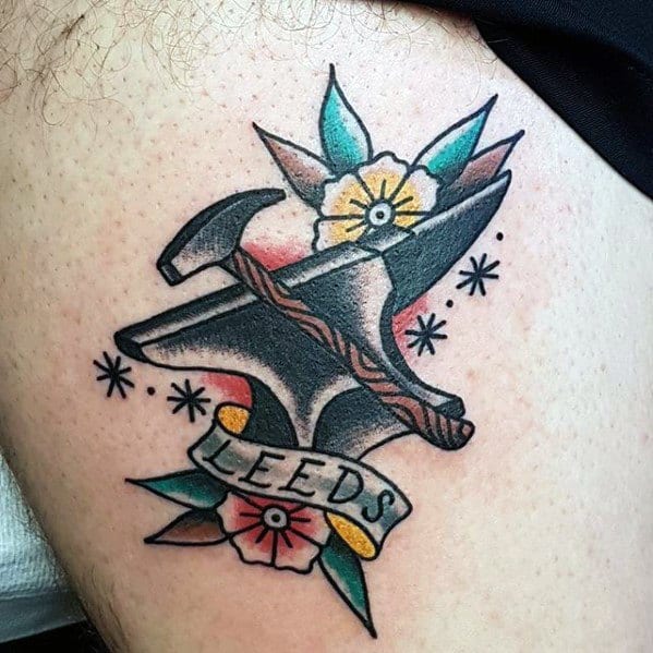 Traditional anvil and hammer tattoo with colorful flowers, stars, and a banner reading "LEEDS," combining classic blacksmith imagery with personal flair.