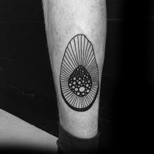 Geometric blackwork avocado tattoo on the calf, featuring bold lines and dot patterns radiating from a stylized seed for a modern look.