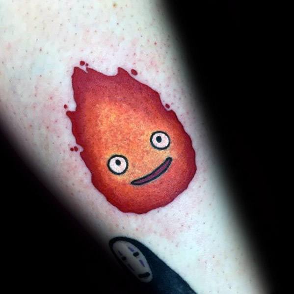 Simple Calcifer tattoo with soft red-orange gradient, a gentle smile, and round eyes, placed near a No-Face tattoo.