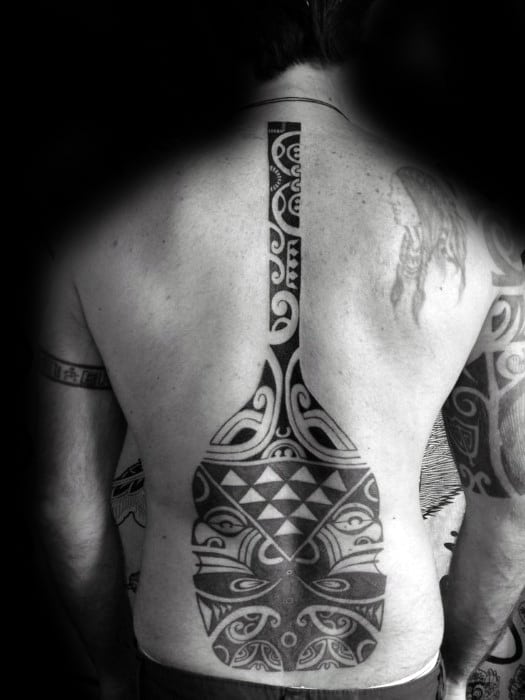 Alt text: Bold and intricate black and grey tattoo of a canoe paddle spanning across the back, featuring Polynesian-inspired tribal patterns.