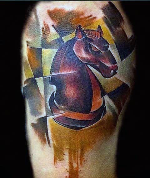 Cubist-style tattoo of a chess knight piece in bold brown and orange tones, with fragmented geometric background on the upper arm.