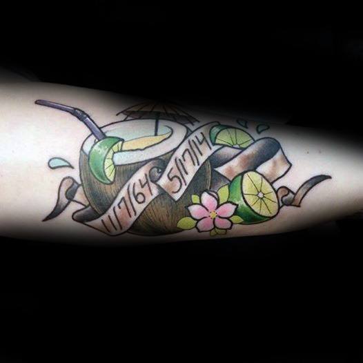 Colorful tattoo of a coconut drink with straw, lime slices, flower, umbrella, and a ribbon featuring dates, placed on the inner arm.