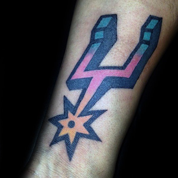 San Antonio Spurs logo tattoo with bold black outline, teal and pink accents, and orange spur design on inner forearm.