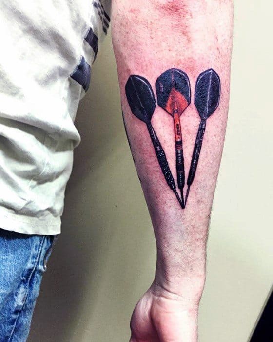 Forearm tattoo of three black darts arranged in a fan shape, with the center dart glowing red, symbolizing passion and precision.