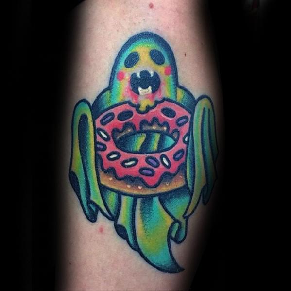 Tattoo of a cute green ghost with blushing cheeks holding a pink frosted donut, blending spooky and sweet in a playful style.