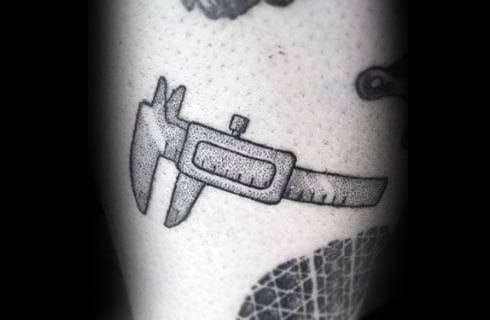 Tattoo of a small vernier caliper in black and gray, representing precision and engineering, inked with subtle dotwork shading.