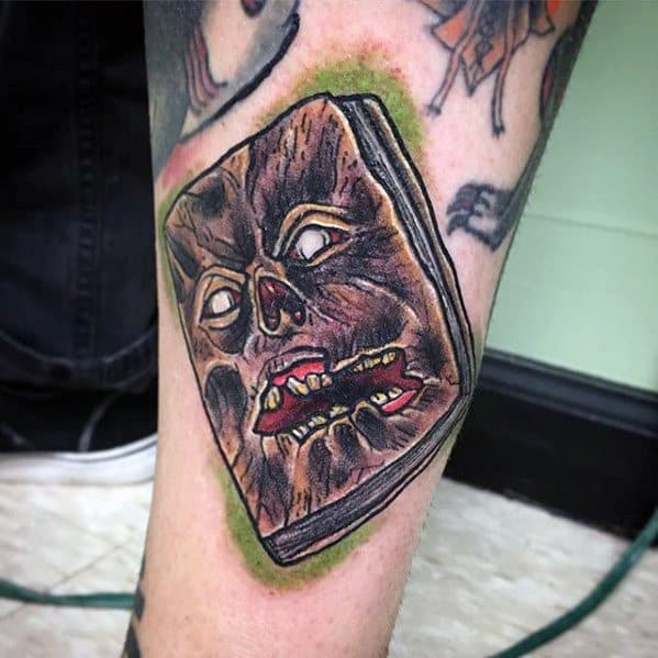 Evil Dead tattoo of the Necronomicon with a snarling face, glowing eyes, and green aura, designed in a bold, comic-horror style