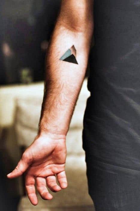 Small geometric mountain tattoo with black and teal shading, placed on the inner forearm for a subtle modern look.