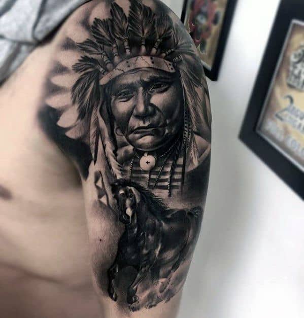 Black and grey tattoo of a Native American chief in a feathered headdress with a galloping horse below on the upper arm