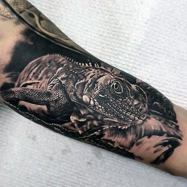 Hyper-realistic black and grey iguana tattoo on forearm with intricate scale detailing and lifelike texture resting on a rock