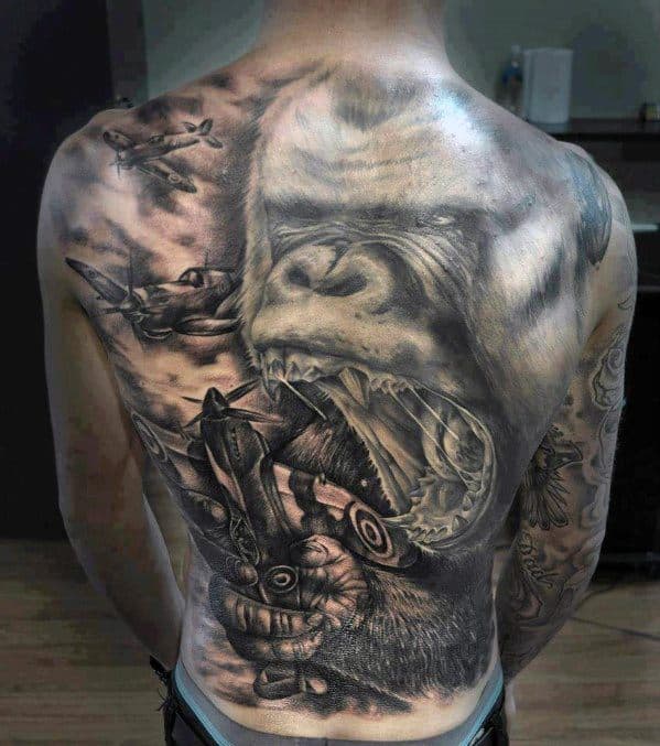 Massive black and grey King Kong back tattoo showing a roaring Kong crushing a fighter plane in his hand while more planes fly overhead.