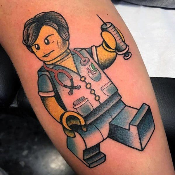 Colorful tattoo of a Lego nurse or doctor holding a syringe, with a stethoscope and medical details on the outfit, done in bold cartoon style.