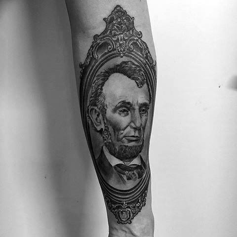 Tattoo of Abraham Lincoln framed with ornate design on a person's forearm