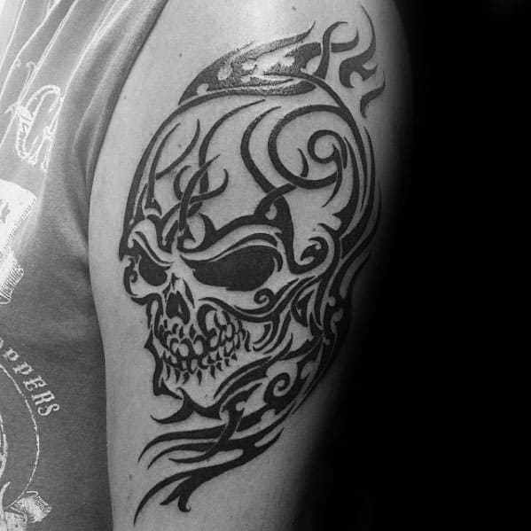 Tribal skull tattoo on upper arm with bold black flames and swirling patterns forming a fierce, stylized skull design.