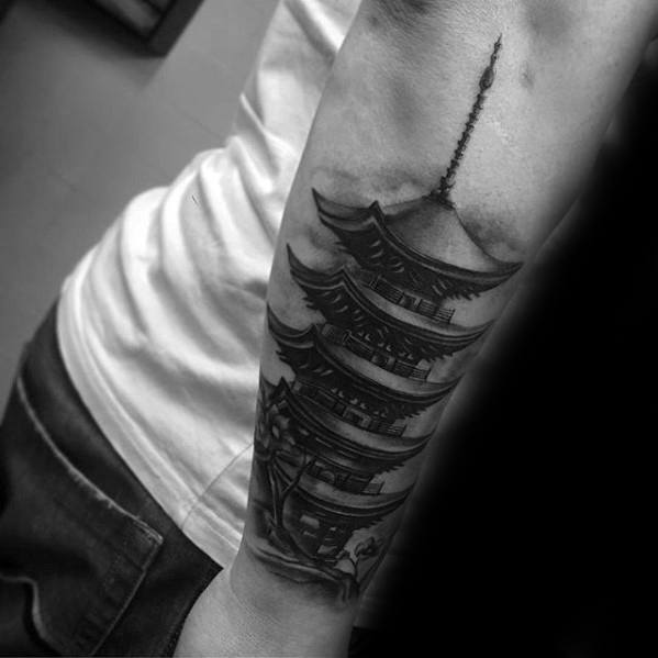 Black and grey forearm tattoo of a tall Japanese pagoda with fine shading, dramatic shadows, and realistic architectural details.