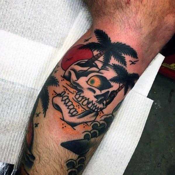 Colorful tattoo of a skull with palm trees, ocean waves, and a red sun on a person's leg