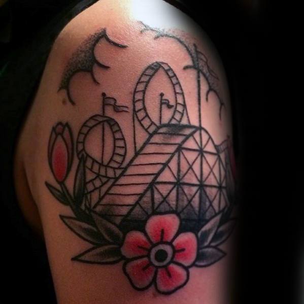 Traditional-style roller coaster tattoo with bold outlines, floral accents, flags, and flying birds on the upper arm.