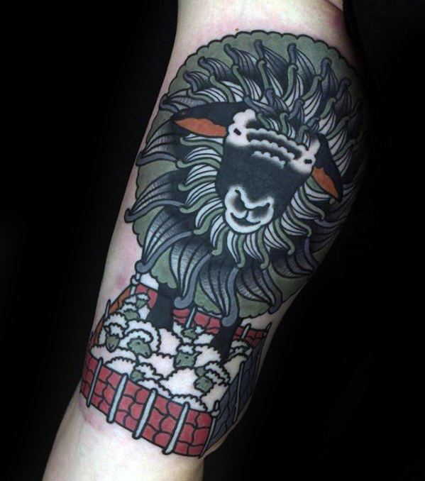 Tattoo on forearm featuring a large black sheep standing over a pen filled with smaller sheep, done in bold, traditional colors.
