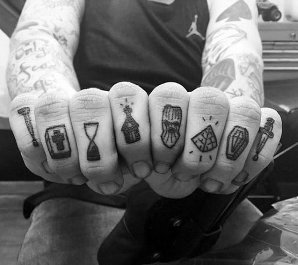 Set of small tattoos across knuckles featuring symbols like a nail, cross, hourglass, bottle, ski mask, pizza slice, coffin, and dagger.