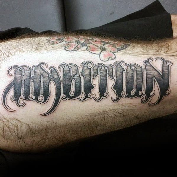 Tattoo with "AMBITION" in bold, ornate font on an arm, enhanced by an elegant floral design