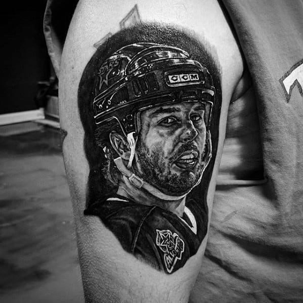 Realistic black and grey tattoo of a hockey player in full gear, featuring detailed facial expression and helmet with team logos