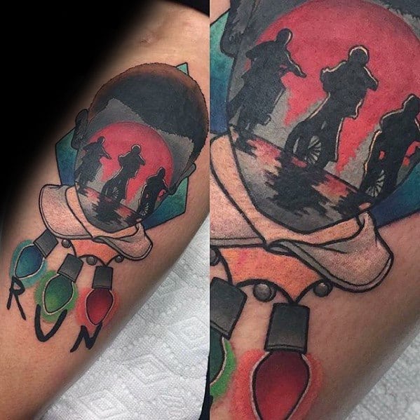 Colorful Stranger Things tattoo of Eleven’s silhouette filled with kids biking at sunset, with “RUN” and holiday lights below.