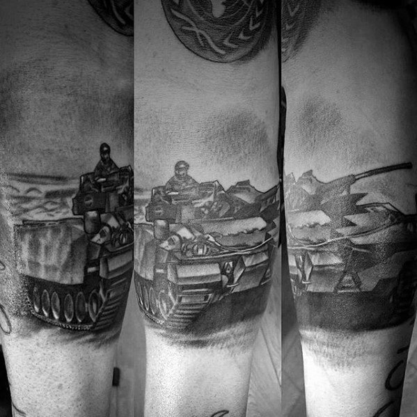 Black and grey arm tattoo of a modern tank in motion with two soldiers onboard, detailed shading and desert backdrop for depth.
