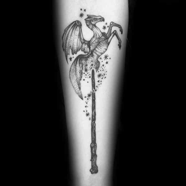 Thestral tattoo above a wand surrounded by sparkles and stars, blending magical and mythical elements on the forearm.