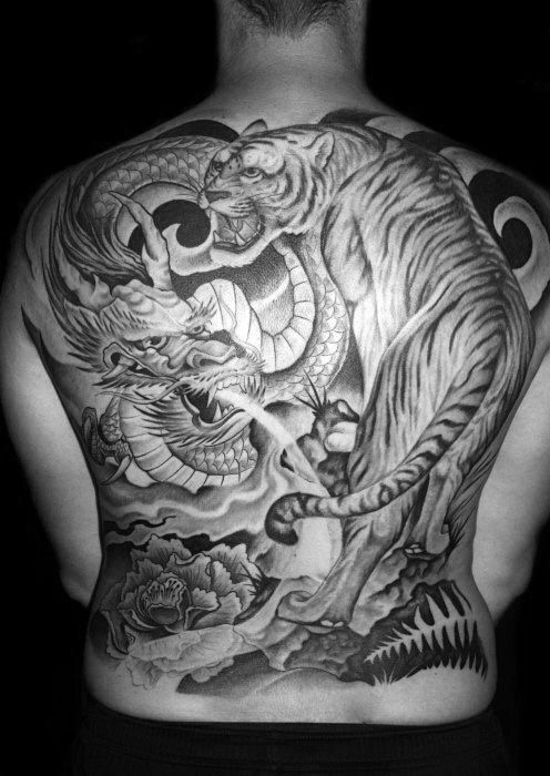 A detailed back tattoo featuring a tiger, dragon, and flowers in black and gray ink