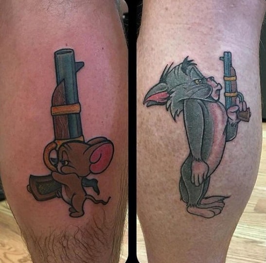 Matching calf tattoos of Jerry holding a gun on one leg and Tom shocked with the barrel in his mouth on the other, in classic cartoon style.
