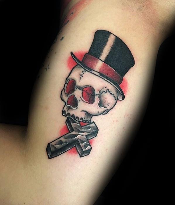 Tattoo of a skull wearing a black top hat with red glasses, placed above a 3D cross, with red shading in the background.