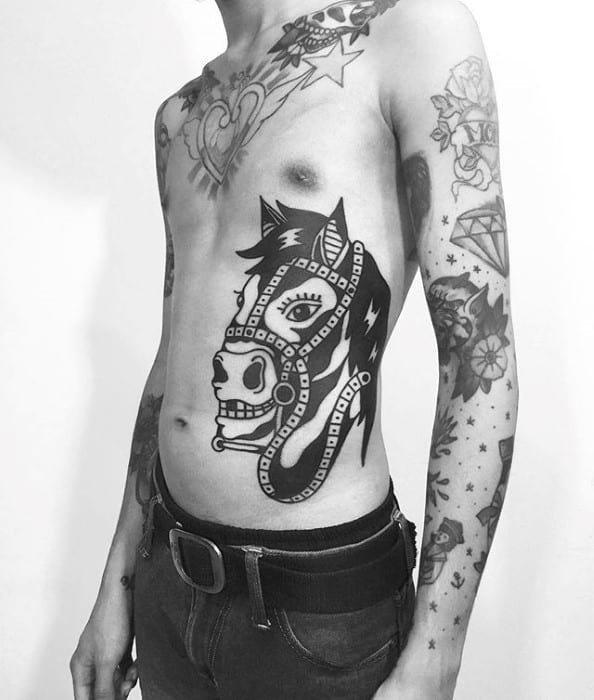 Large side tattoo of a stylized horse skull in bold black ink with harness details, placed prominently on the ribcage and torso.