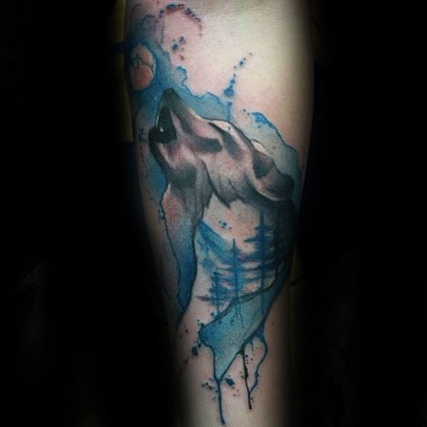Howling wolf tattoo with blue watercolor splashes, moon, and forest silhouettes, blending nature and emotion in a dreamy design.