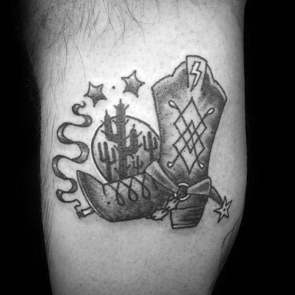 Black and white tattoo of a cowboy boot with desert scenery, stars, and a lightning bolt, symbolizing Western adventure and rugged independence.