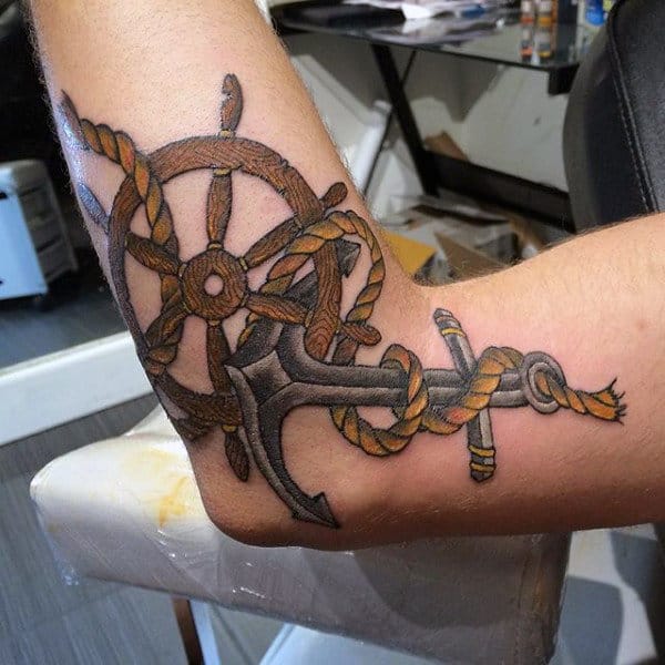 Male With Elbow Tattoo Of Ship Wheel And Anchor