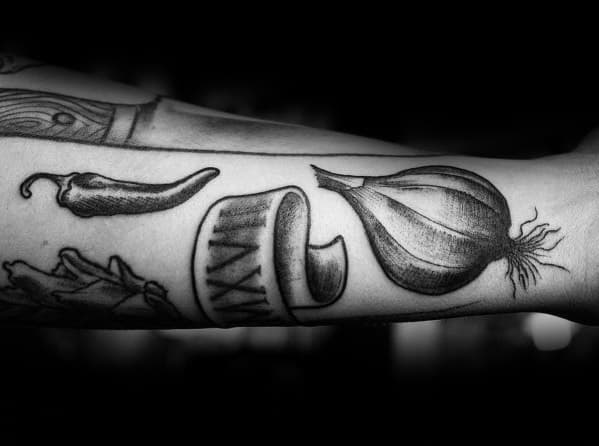 Black and grey garlic tattoo on the forearm with fine shading, paired with chili and other culinary elements for a bold and artistic design.
