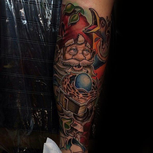 Tattoo of a mystical gnome with a red hat and white beard, holding a glowing blue orb in a nest, surrounded by vibrant leaves and a bird.