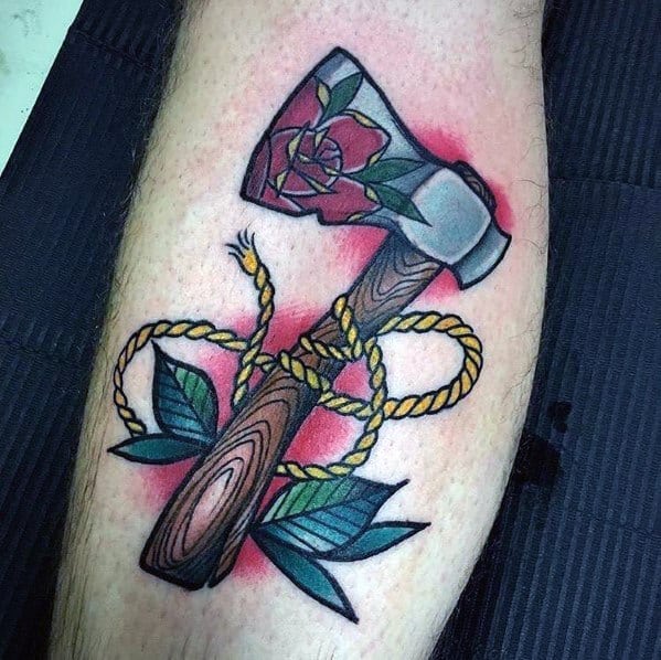 Colorful hatchet tattoo with a wood-textured handle, a floral design on the blade, a coiled golden rope, and green leaves, set against red shading.